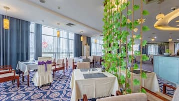 A hotel dining area with tables set for guests, a reception desk, and a large window with a view.
