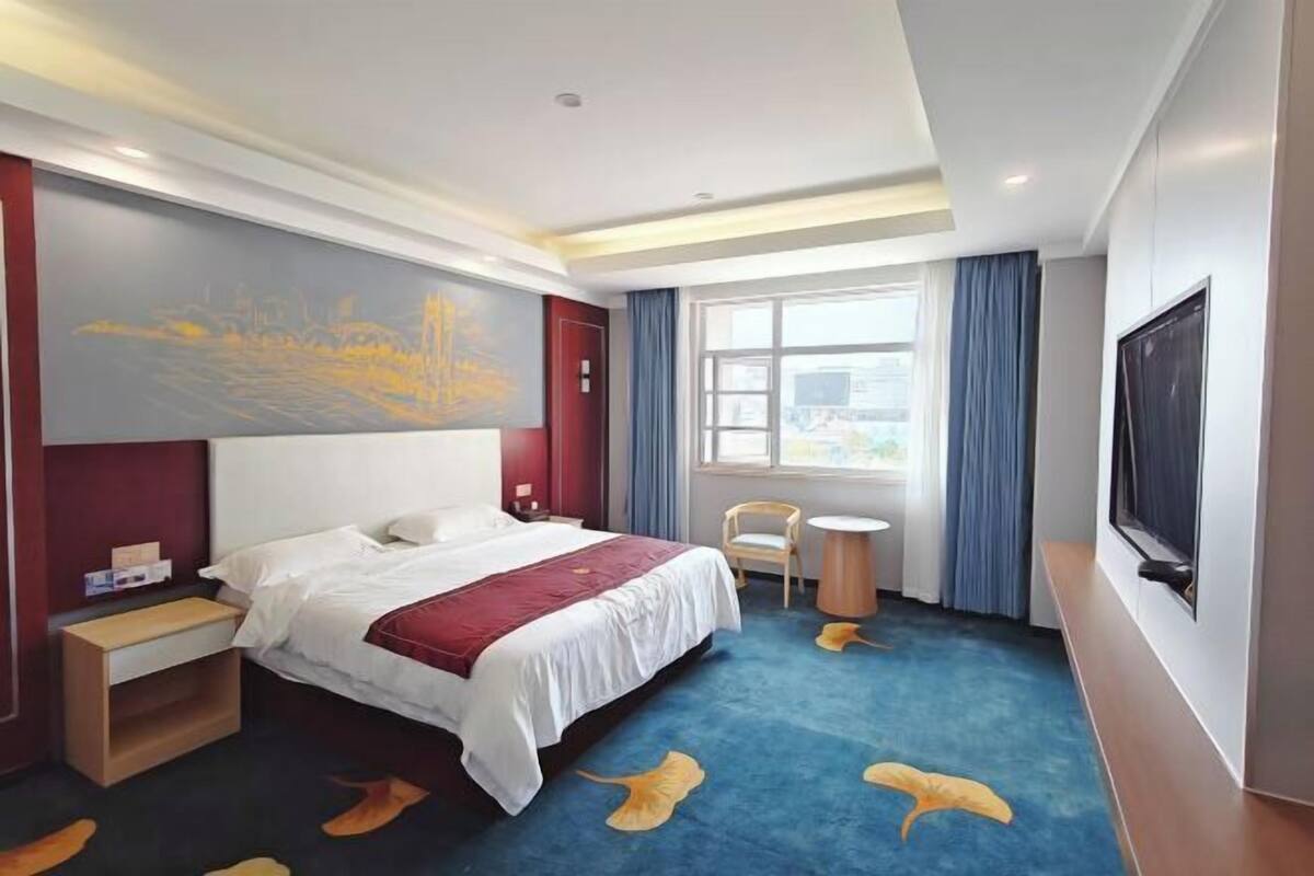 A hotel room with a bed, a desk, a chair, a television, and a window.