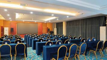 A conference room with rows of tables and chairs, a projector screen, and a stage.