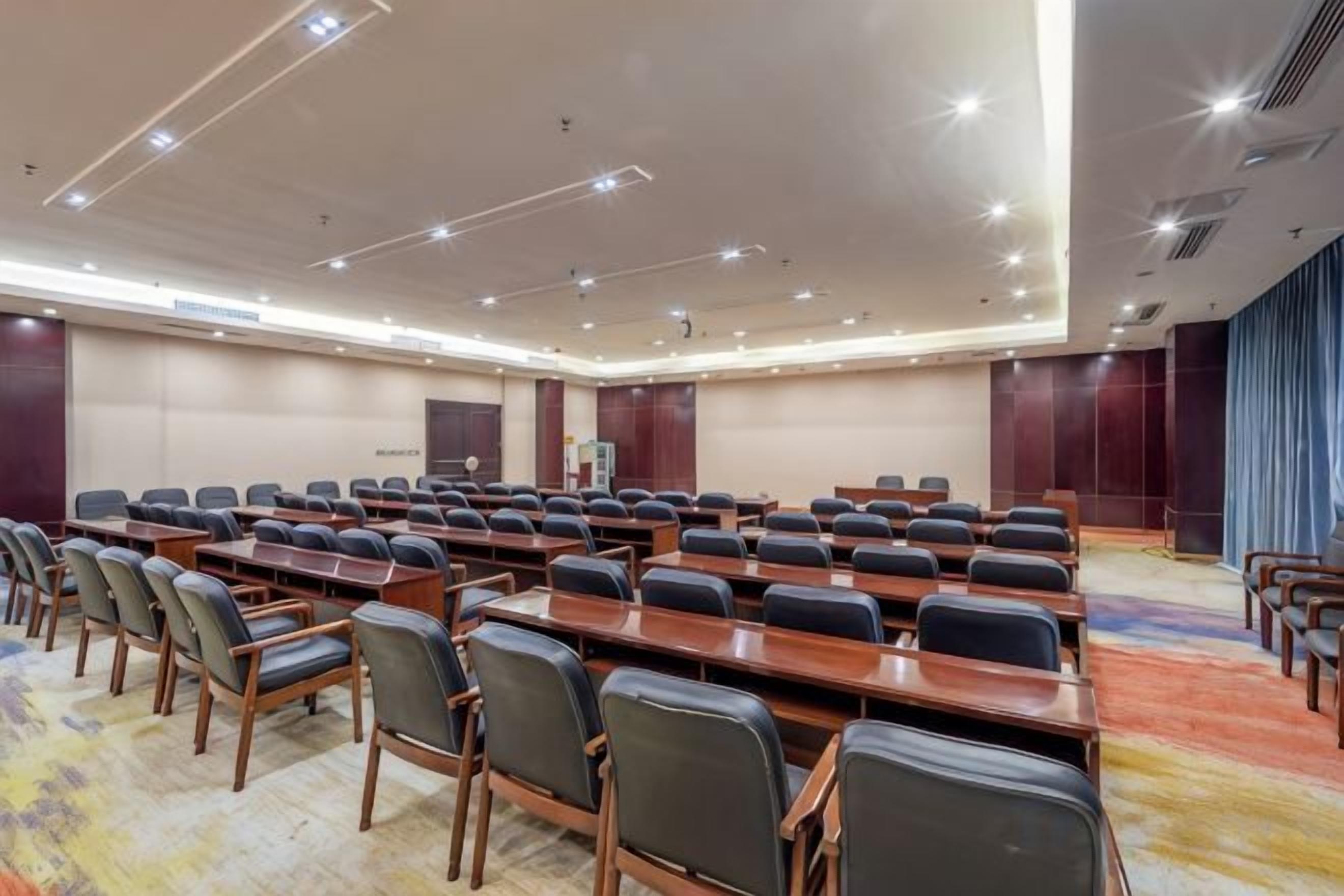 A conference room with rows of tables and chairs, a carpeted floor, and a large window with curtains.