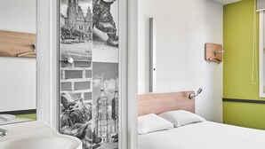 Habitación de hotel moderna con cama, baño con lavamanos y ventana grande con vistas a un edificio histórico.