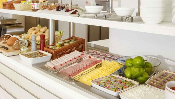 Un bufé con diferentes opciones de comida, incluyendo pan, pasteles, carnes, quesos y salsas.