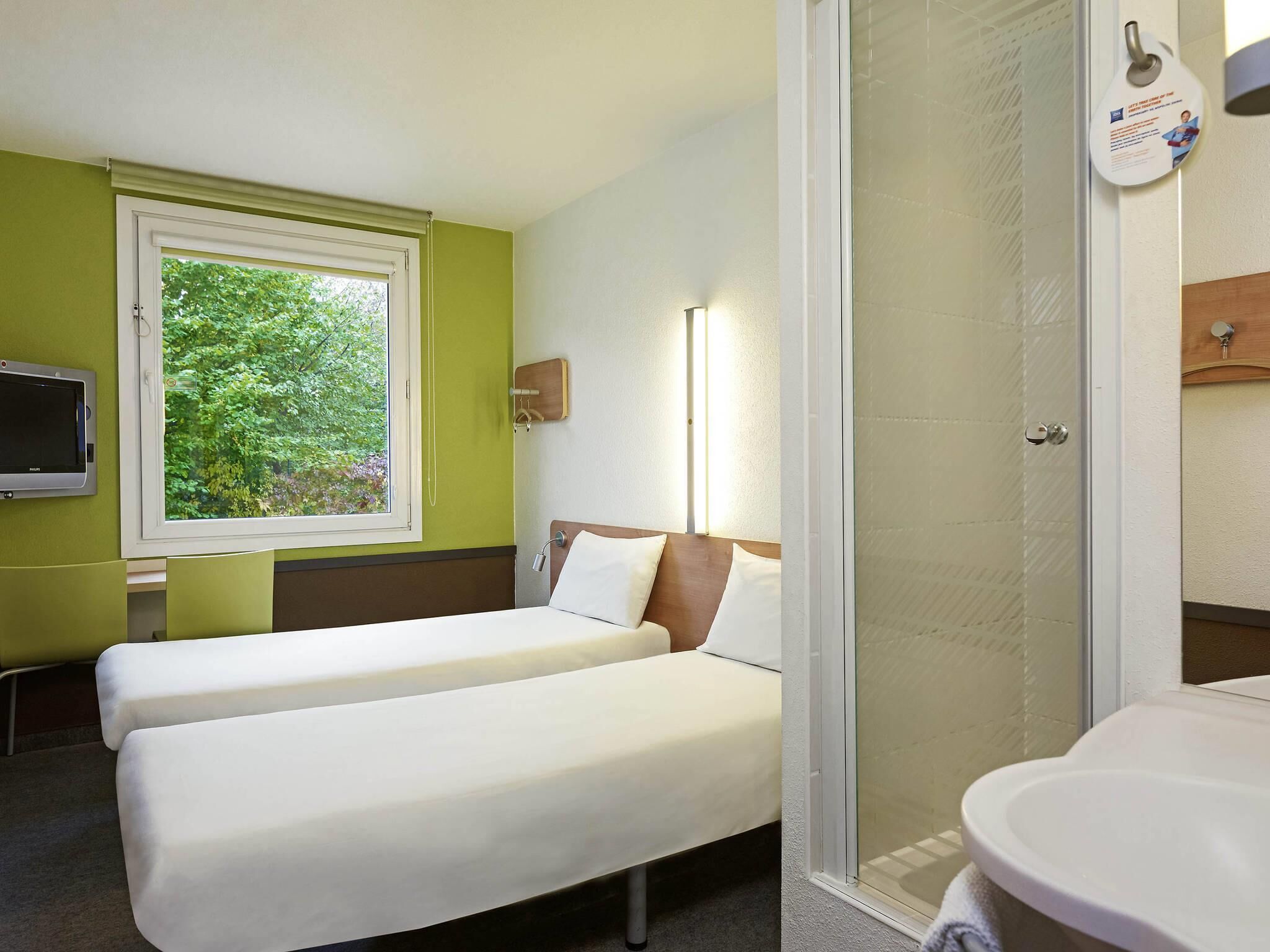 Ein Hotelzimmer mit einem Bett, einem Fernseher, einem Fenster mit Blick auf Bäume und einem Duschbereich.