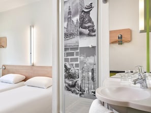 A hotel room with a bed, a bathroom with a sink and mirror, and a wall with a photo collage. - Ibis Budget Wroclaw Poludnie (Wroclaw)