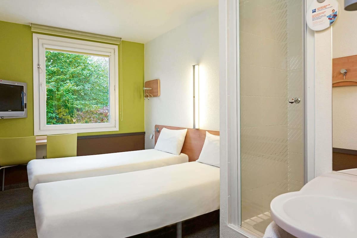 Ett hotellrum med en sÀng, en tv, ett fönster med utsikt över grönomrÄden och en dusch.