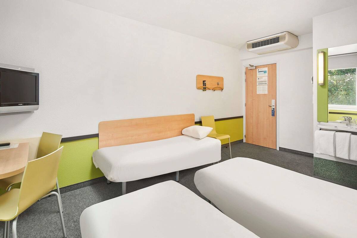 A hotel room with two beds, a desk, a chair, a TV, a door, and a window.
