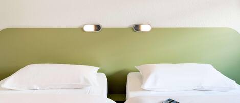 A hotel room with two beds, white bedding, a green headboard, and a wall-mounted light fixture.