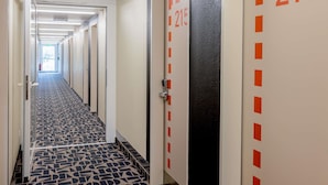 Un couloir d’hôtel avec des portes numérotées 215 et 217, une moquette à motifs et un plafond éclairé par des néons.