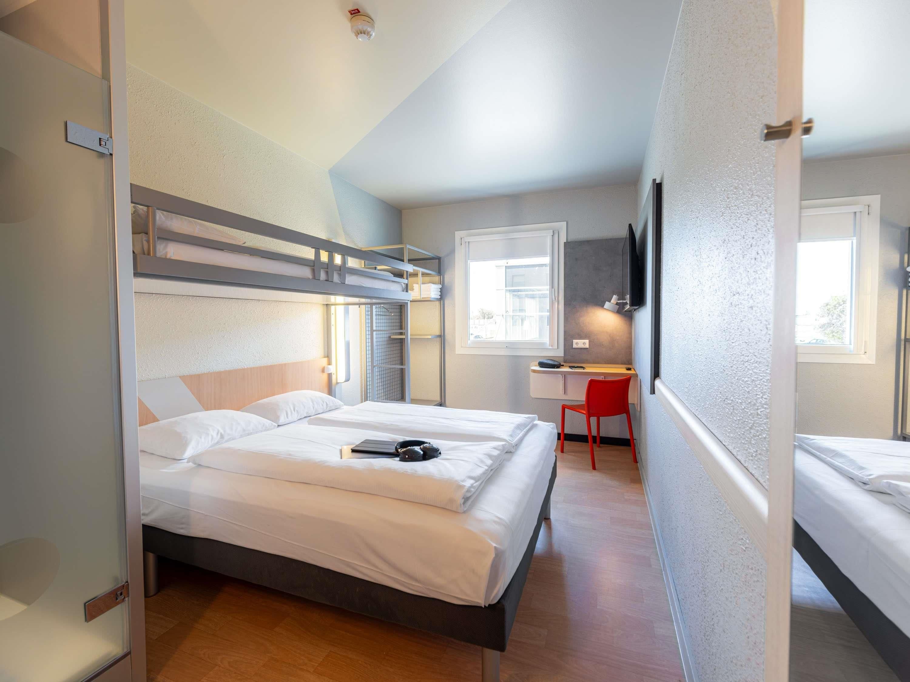 Una habitación de hotel compacta con una cama litera, un escritorio, una silla y un televisor.