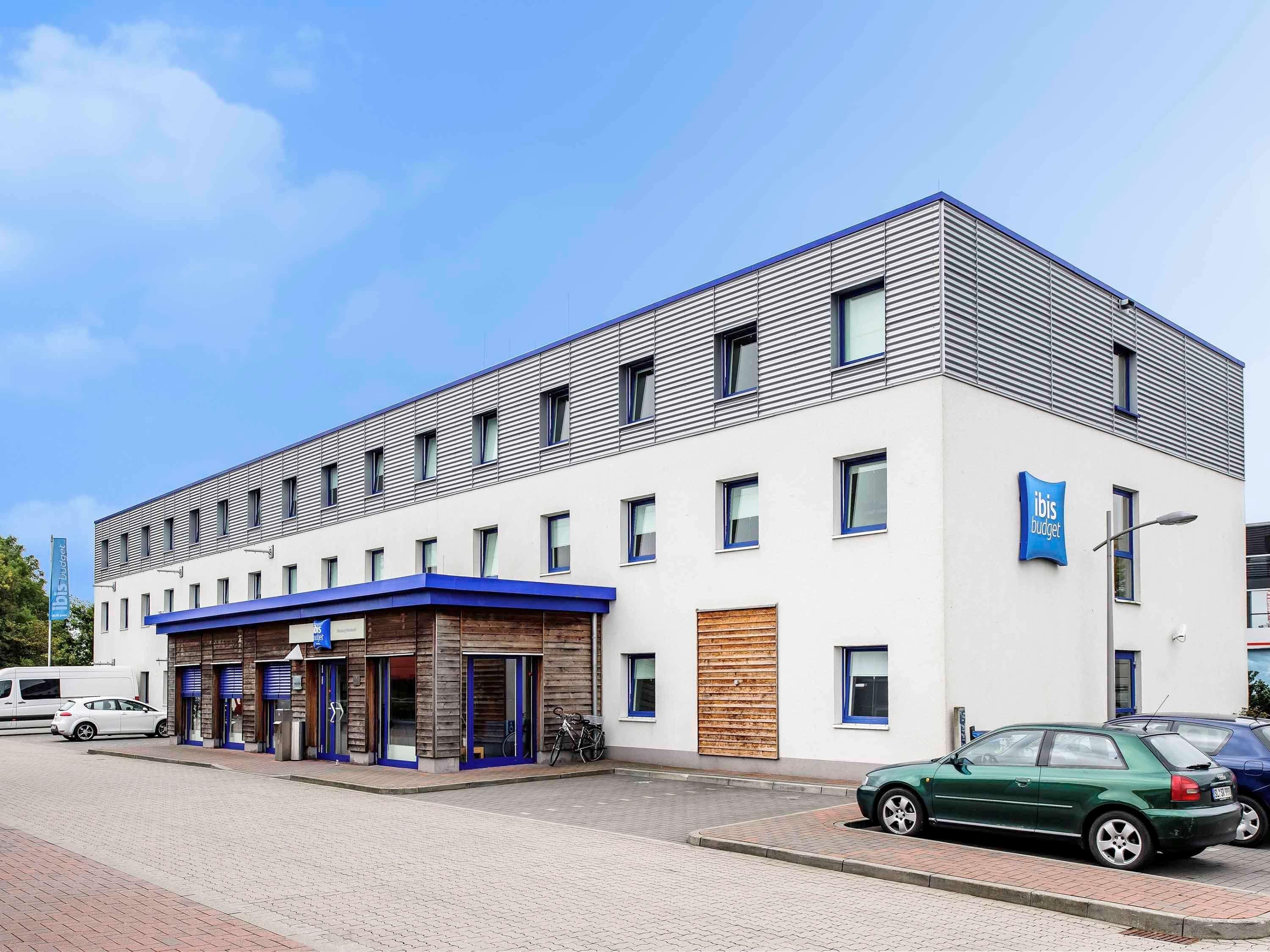A modern building with a flat roof, multiple windows, and a blue awning over the entrance.