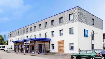 A modern building with a flat roof, multiple windows, and a blue awning over the entrance.