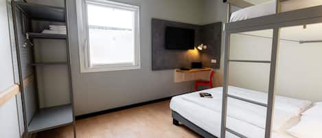Ein kleines Zimmer mit Etagenbett, Schreibtisch mit Stuhl, Wand-Fernseher und einem Fenster für Tageslicht.