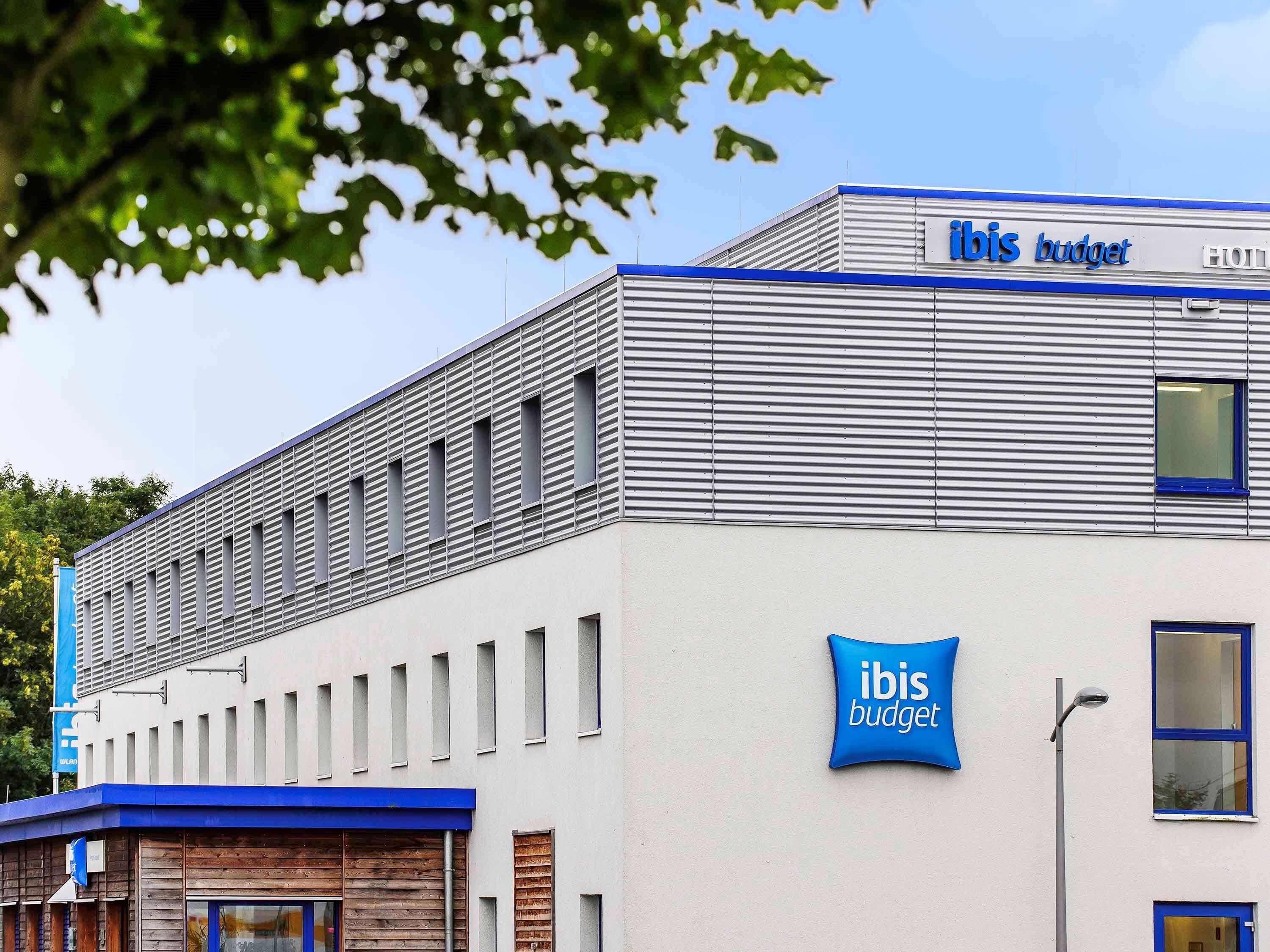 Ein Gebäude mit moderner Fassade, einem gut sichtbaren 'ibis budget'-Schild und einer Reihe von Fenstern.