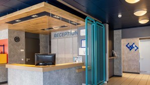 A reception desk with a computer, a clock, and a sign indicating the reception area. - Ibis Budget Flensburg Handewitt (Handewitt)