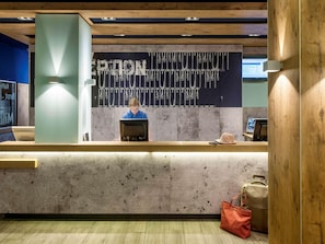 A reception desk with a modern design, featuring a wooden counter and a large screen displaying information. - Ibis Budget Flensburg Handewitt (Handewitt)
