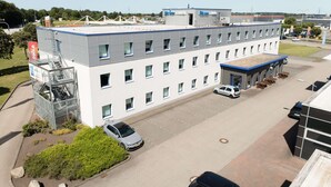 A multi-story building with a parking lot, a covered outdoor seating area, and a staircase leading to an upper level. - Ibis Budget Flensburg Handewitt (Handewitt)