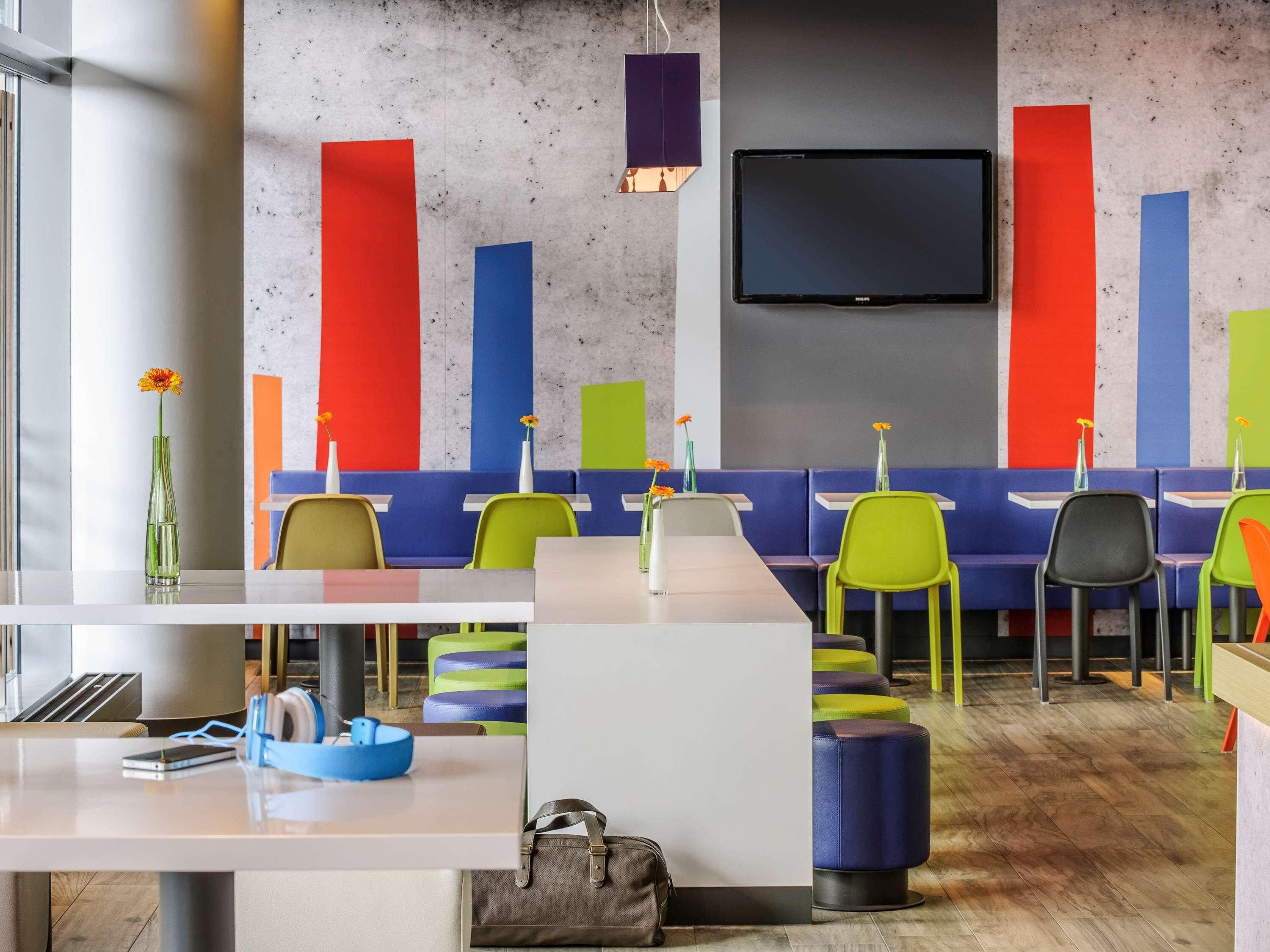 Un interior de restaurante moderno con asientos coloridos, un televisor de pantalla plana y una barra blanca.