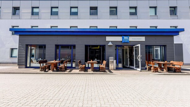 A modern hotel with a blue awning, outdoor seating, and a sign indicating it's an ibis budget hotel. - Ibis Budget Flensburg Handewitt (Handewitt)