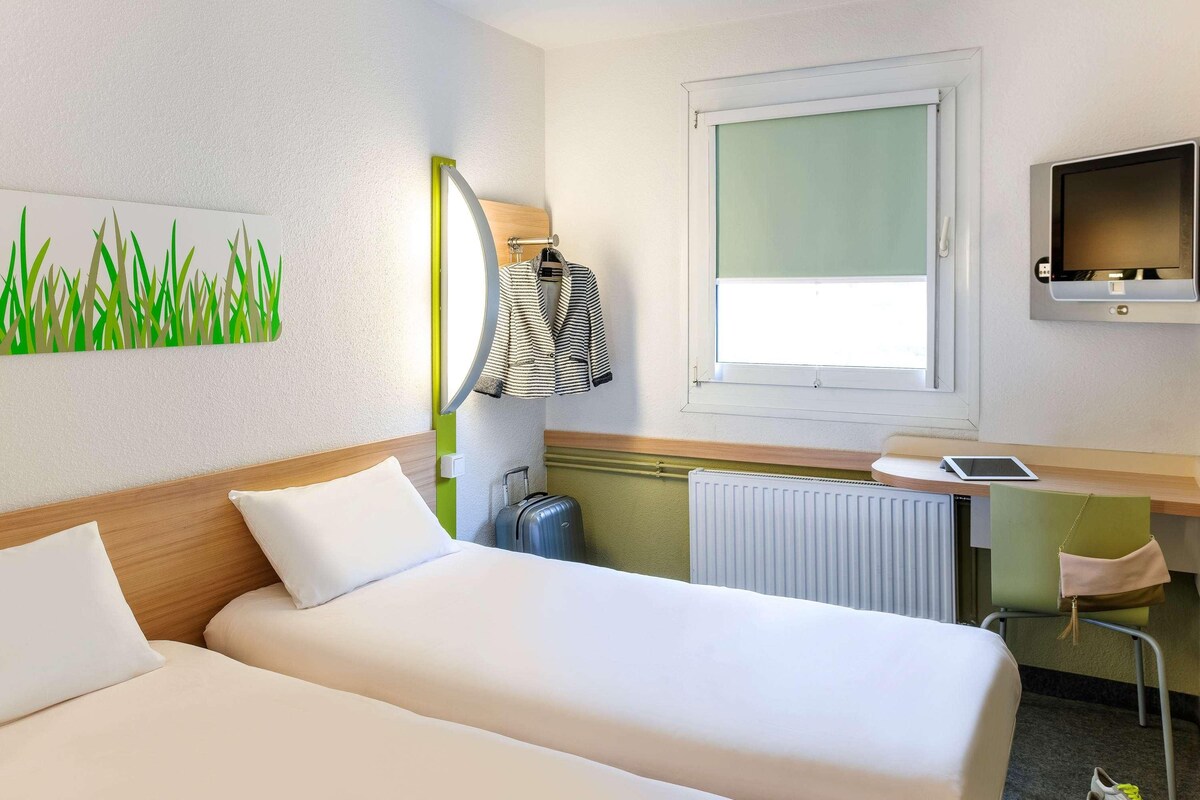 A hotel room with two beds, a desk with a computer, a TV, and a window with a view.