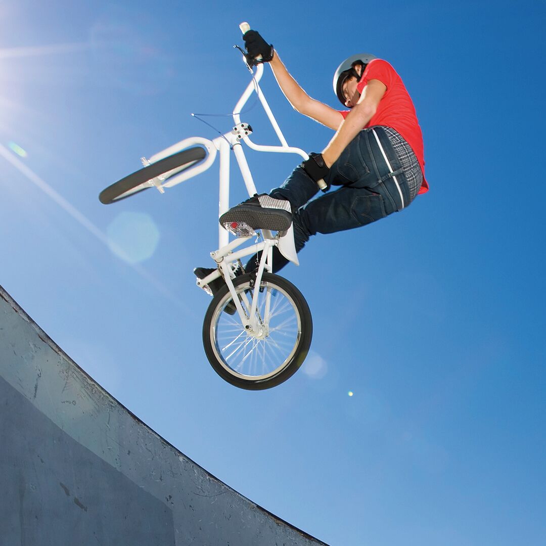 A person performing a BMX stunt on a white bike at a skatepark.