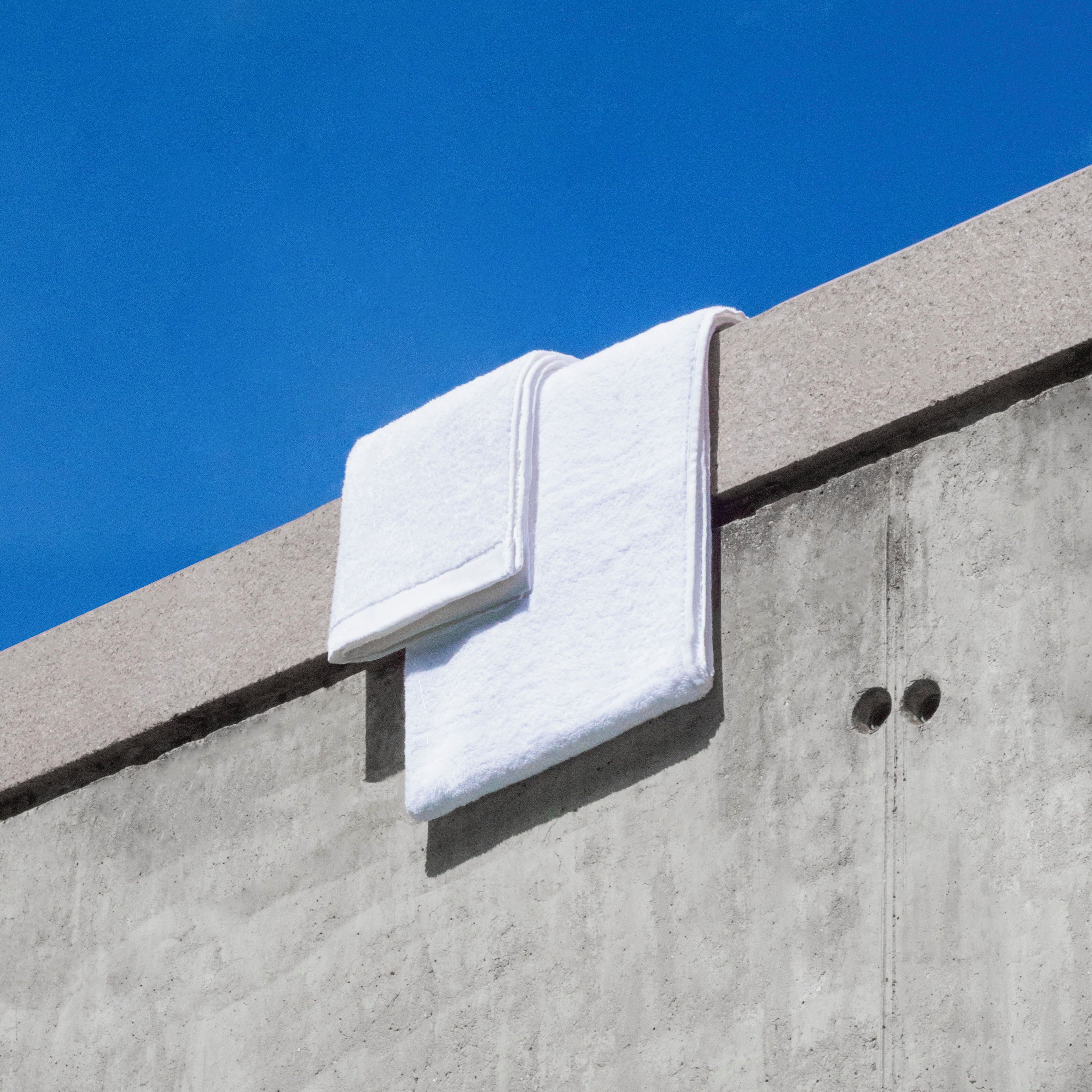 Un asciugamano bianco appeso a una parete in cemento, con un cielo azzurro sullo sfondo.