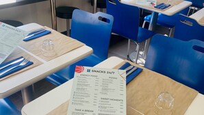 Un ristorante con sedie e tavoli blu, menù e una finestra con piante.