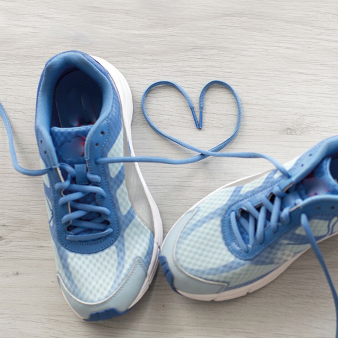 Blaue und weiße Sneaker mit herzförmig gebundenen Schnürsenkeln auf Holzdielen.