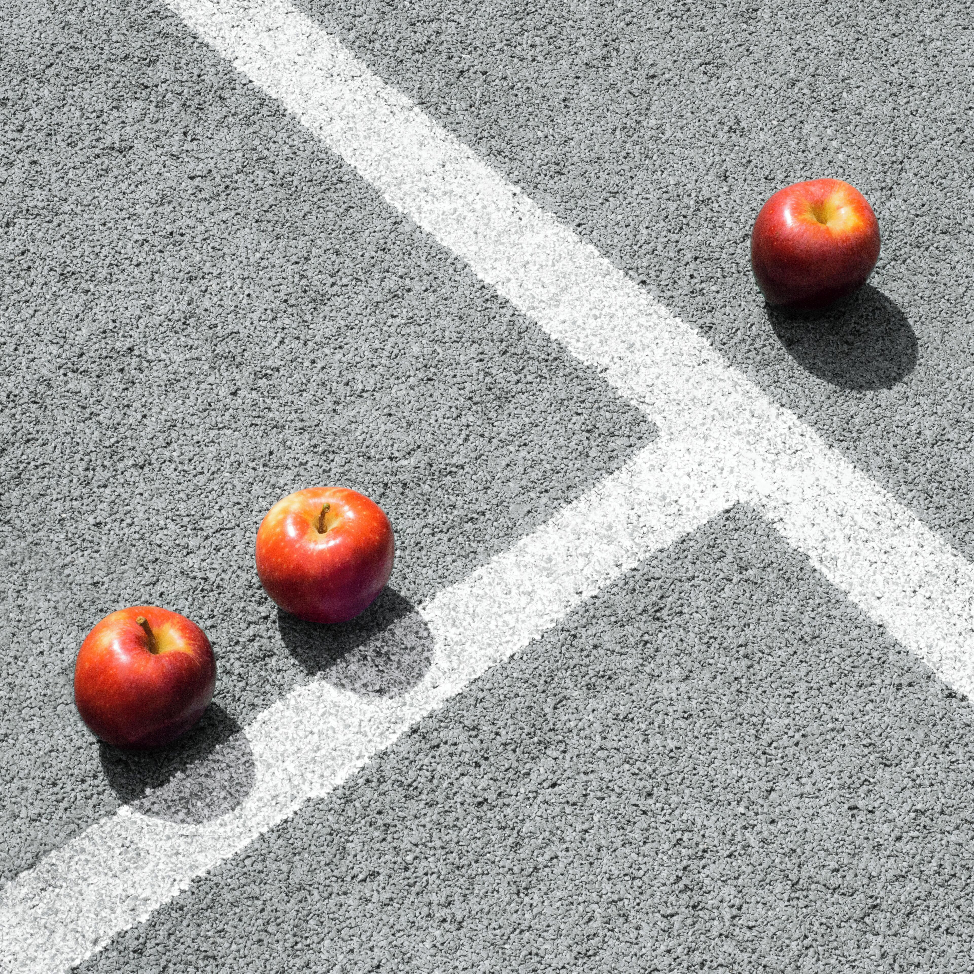 Three apples on a road with white markings.