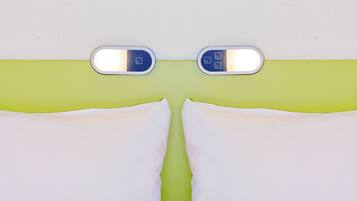 Ein Zimmer mit Grün-Weiß-Farbgestaltung, einem Bett mit weißer Bettwäsche und einem an der Wand montierten Thermostat.