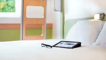 Una cama bien hecha con una tableta y gafas encima, una puerta de madera y una pared verde.