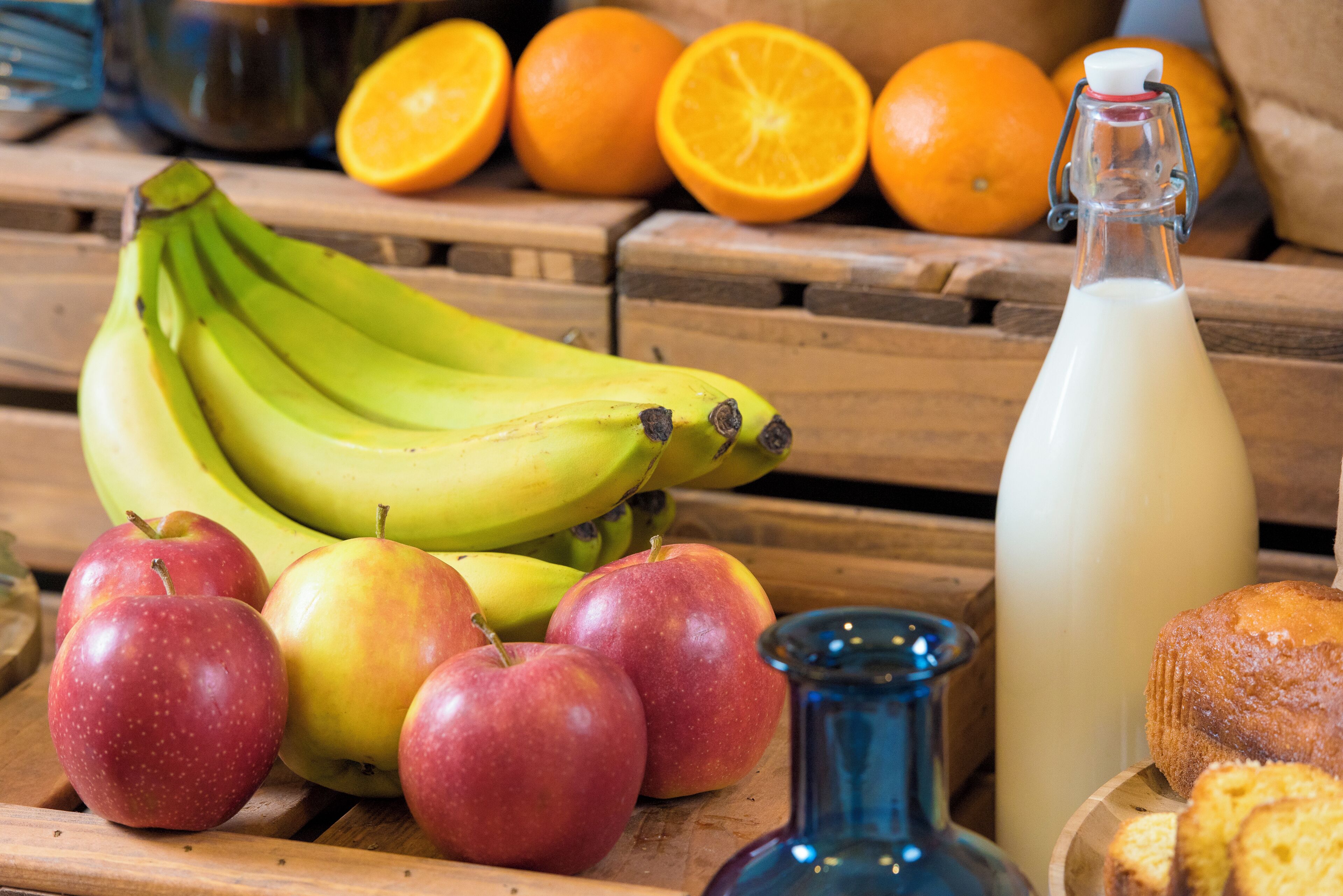 A wooden table with bananas, apples, oranges, a milk bottle, and a blue vase.