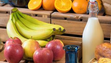 A wooden table with bananas, apples, oranges, a milk bottle, and a blue vase.