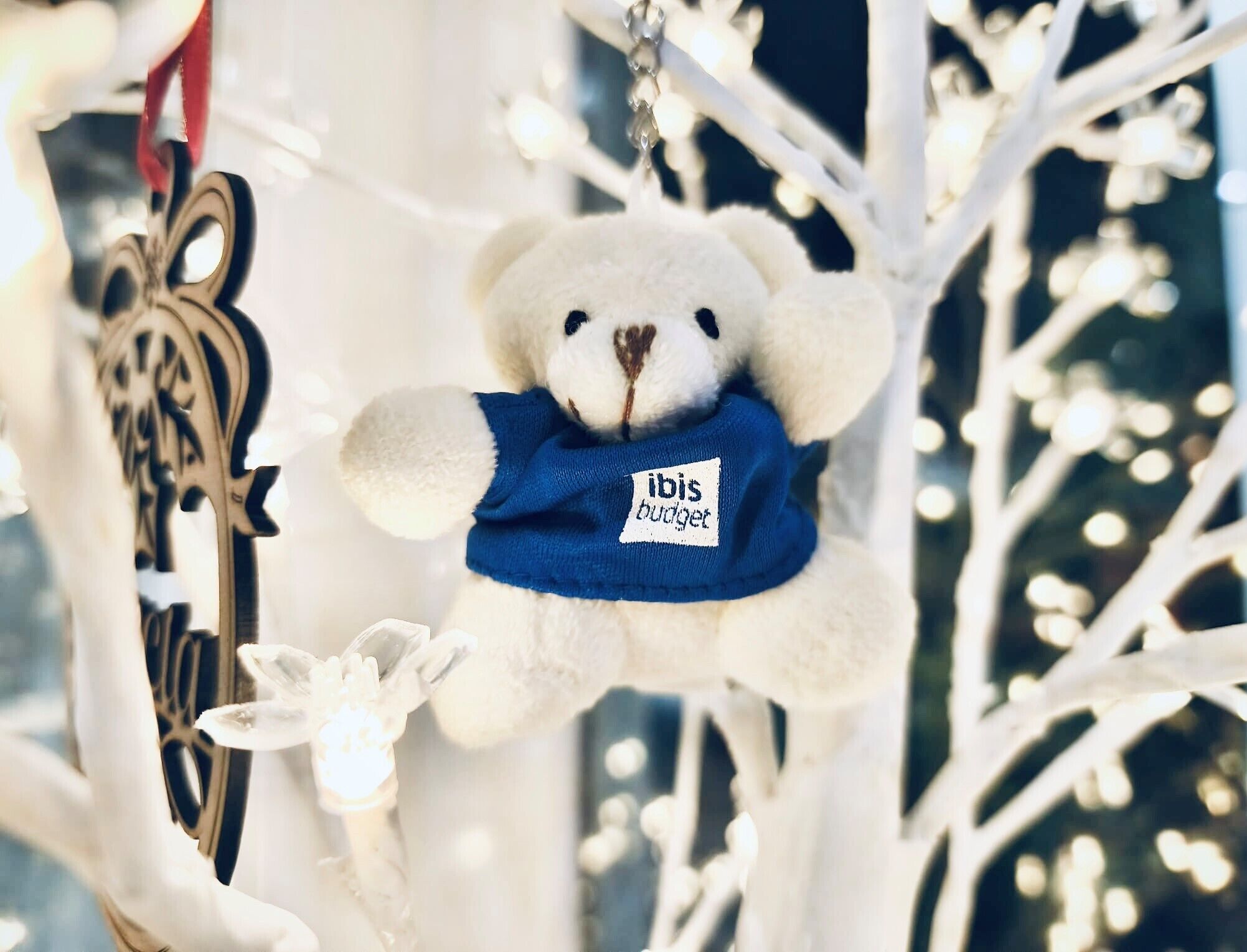 En hvid bamse med et blåt mærke hænger på en hvid juletræ.