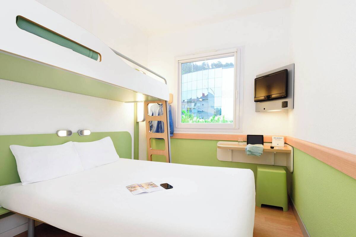 Hotelkamer met een bed, een raam, een televisie en een klein tafeltje met een handdoek en een boek.