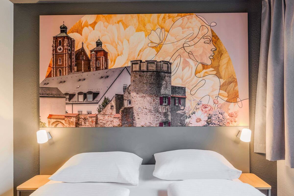A hotel room with a bed, two bedside tables, and a large wall mural depicting a cityscape and a woman's profile.