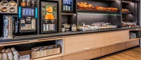 A self-service breakfast station with coffee machines, tea dispensers, and a variety of food options.