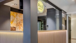 A hotel reception area with a modern design, featuring a reception desk, a large abstract artwork on the wall, and a sign for B&B Hotels. - B&B HOTEL Ingolstadt-Lenting (Lenting)