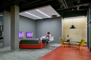 Un espacio lounge moderno con un sofá rojo, dos sillones, una mesa y un ventanal grande.