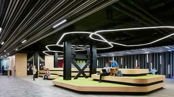 Un intérieur moderne avec un espace salon central, un plafond haut doté d’un éclairage linéaire et un escalier apparent.