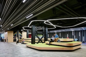 A modern interior with a central seating area, a high ceiling with linear lighting, and a visible staircase.