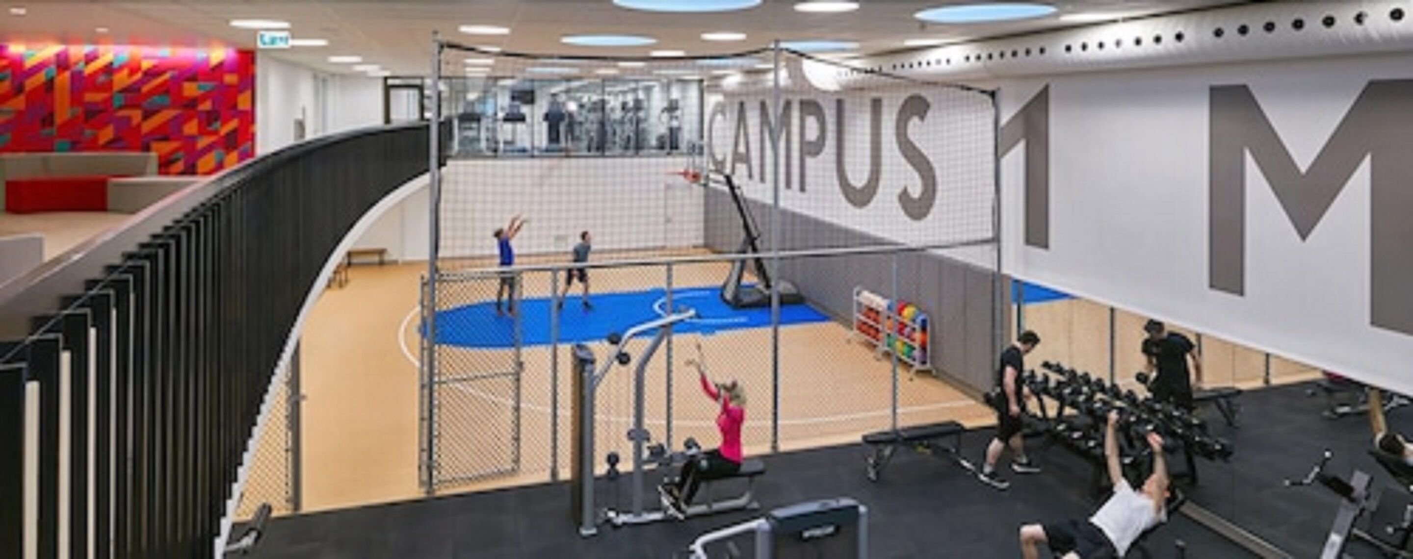 Una palestra con campo da basket, attrezzature per esercizi e un grande cartello con su scritto 'CAMPUS 1'.