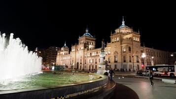 A historic building with a large fountain in front, featuring a circular tiled border and a statue in the center.