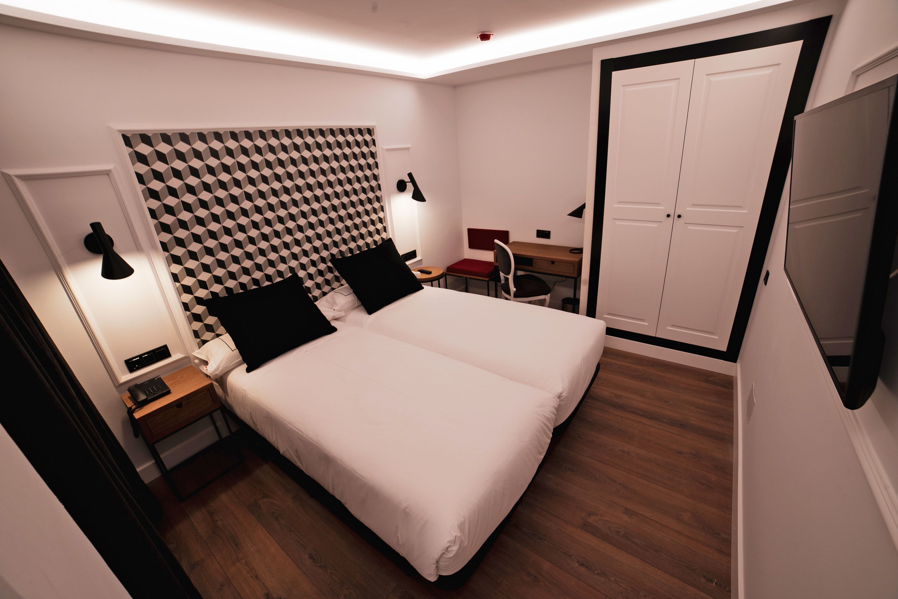 A hotel room with a bed, bedside tables, a desk, and a wardrobe.