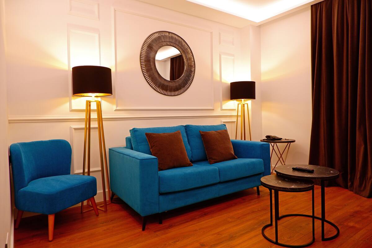 Una habitación con un sofá azul, un sillón a juego, un espejo redondo, dos lámparas de pie y una mesita redonda.