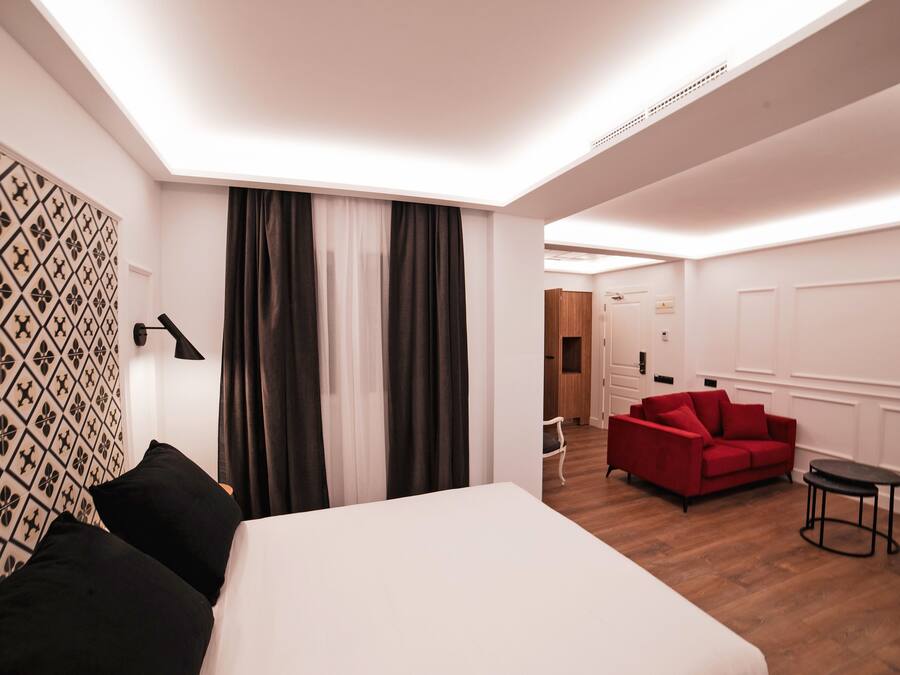 A hotel room with a bed, a red sofa, a small table, and a wall with a geometric pattern.