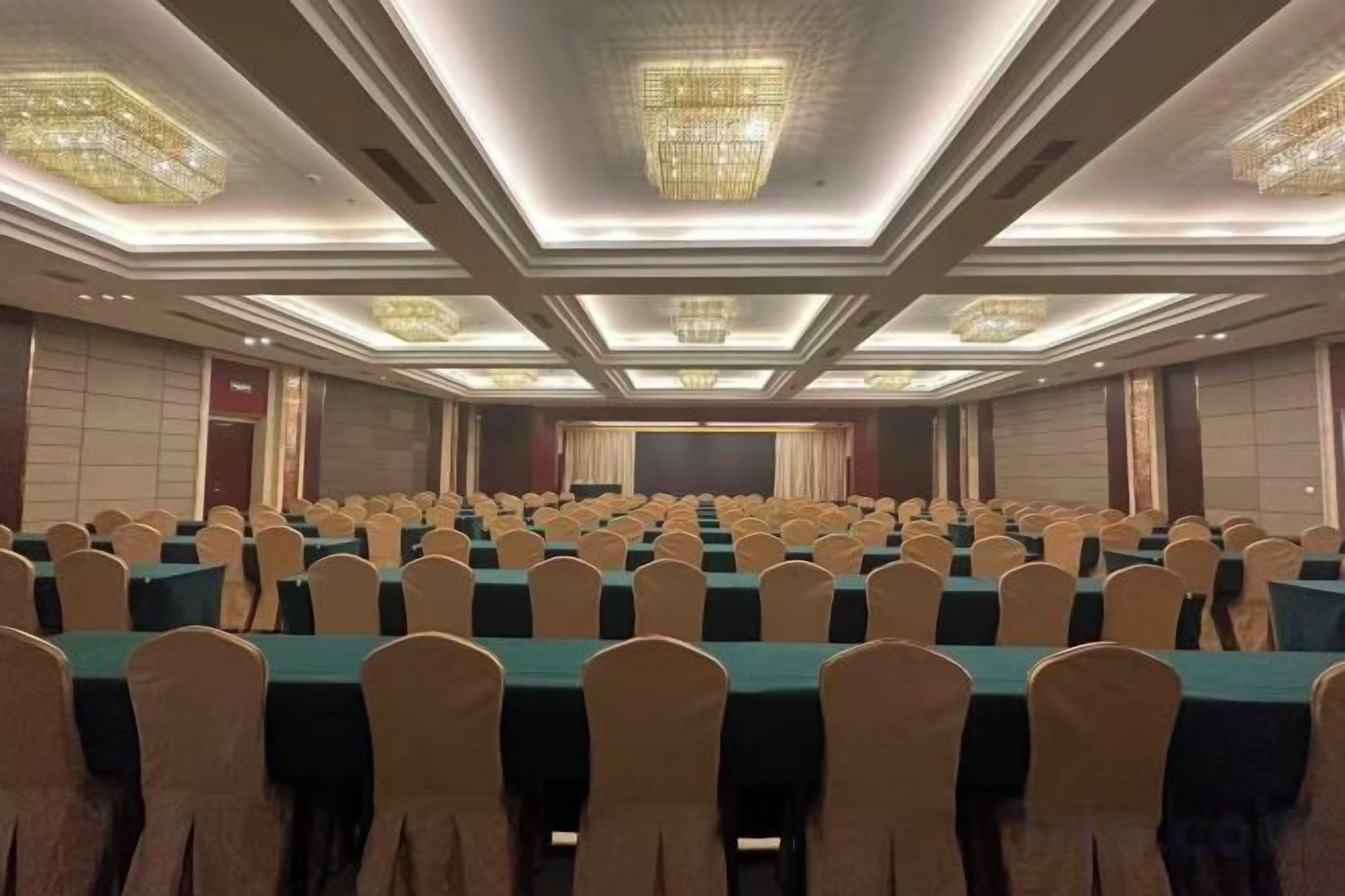 A conference room with rows of tables and chairs, a stage, and a large screen.