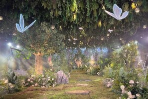 Un jardin avec un sentier, des arbres et des guirlandes lumineuses.
