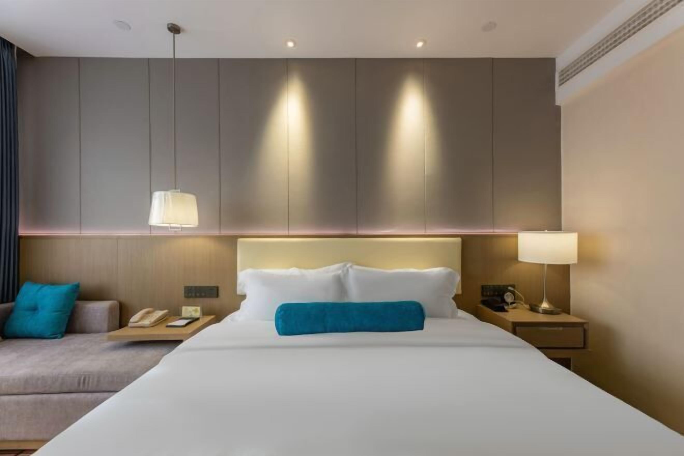 Una habitación de hotel con una cama grande, mesitas de noche, un sofá y una lámpara de pared.