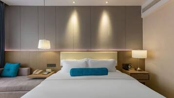 Una habitación de hotel con una cama grande, mesitas de noche, un sofá y una lámpara de pared.