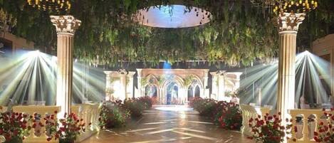 An indoor venue with a central aisle, columns, and floral arrangements.
